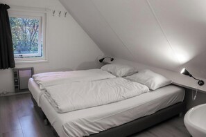 A bedroom with a bed, a window, a radiator, and a bedside table with a lamp. - This 8-person vacation home is fully equipped and the perfect spot for a family vacation. (Hoge Hexel)
