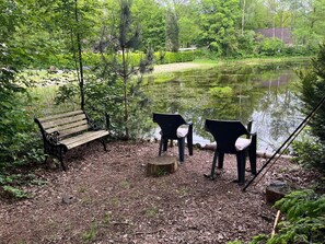 A bench and chairs by a pond with trees and a building in the background. - This 8-person vacation home is fully equipped and the perfect spot for a family vacation. (Hoge Hexel)