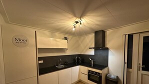 Una cocina compacta con armarios blancos, una encimera negra, horno empotrado, un lavabo y un cubo de basura.
