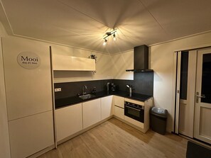Eine kleine Küche mit weißen Schränken, einer schwarzen Arbeitsplatte, einem eingebauten Backofen, einem Spülbecken und einem Mülleimer.