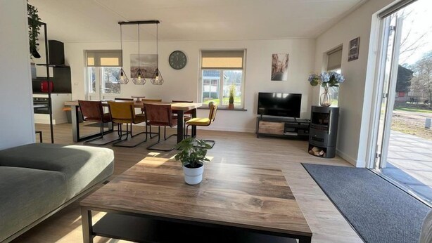 Una sala de estar moderna con un sofá, una mesa de comedor, sillas, un televisor y un amplio ventanal.