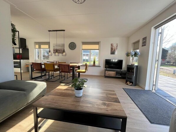 Ein modernes Wohnzimmer mit einer Couch, einem Esstisch, Stühlen, einem Fernseher und einem großen Fenster.