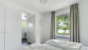 Un dormitorio con dos camas, una ventana con cortinas, una puerta que da a un área de lavandería y una lámpara en el techo.