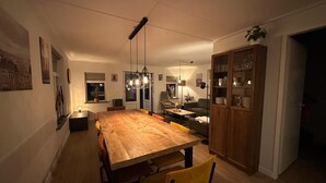 Un comedor con una gran mesa de madera, sillas, luces colgantes y un aparador con cristalería.