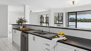 Une cuisine moderne avec un plan de travail noir, des armoires blanches, un lave-vaisselle et une vue sur un lac grâce à de grandes fenêtres.