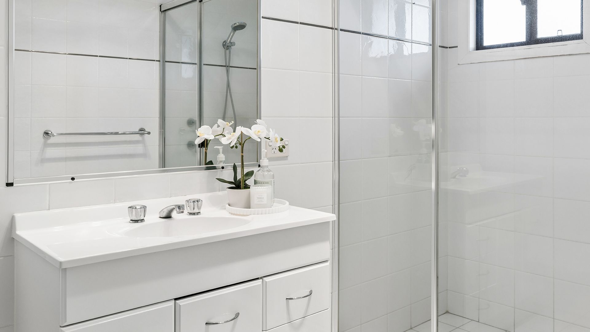 Ein modernes Badezimmer mit einem weißen Waschtisch, einer Duschkabine aus Glas und einem Topf mit einer Orchidee.