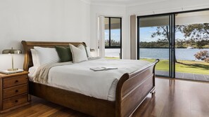 Une chambre à coucher avec un lit en bois, une table de chevet, une lampe et une vue sur un lac, visible à travers une porte coulissante.
