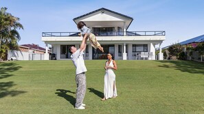 Une maison moderne avec une grande pelouse, un patio couvert et un ciel dégagé.