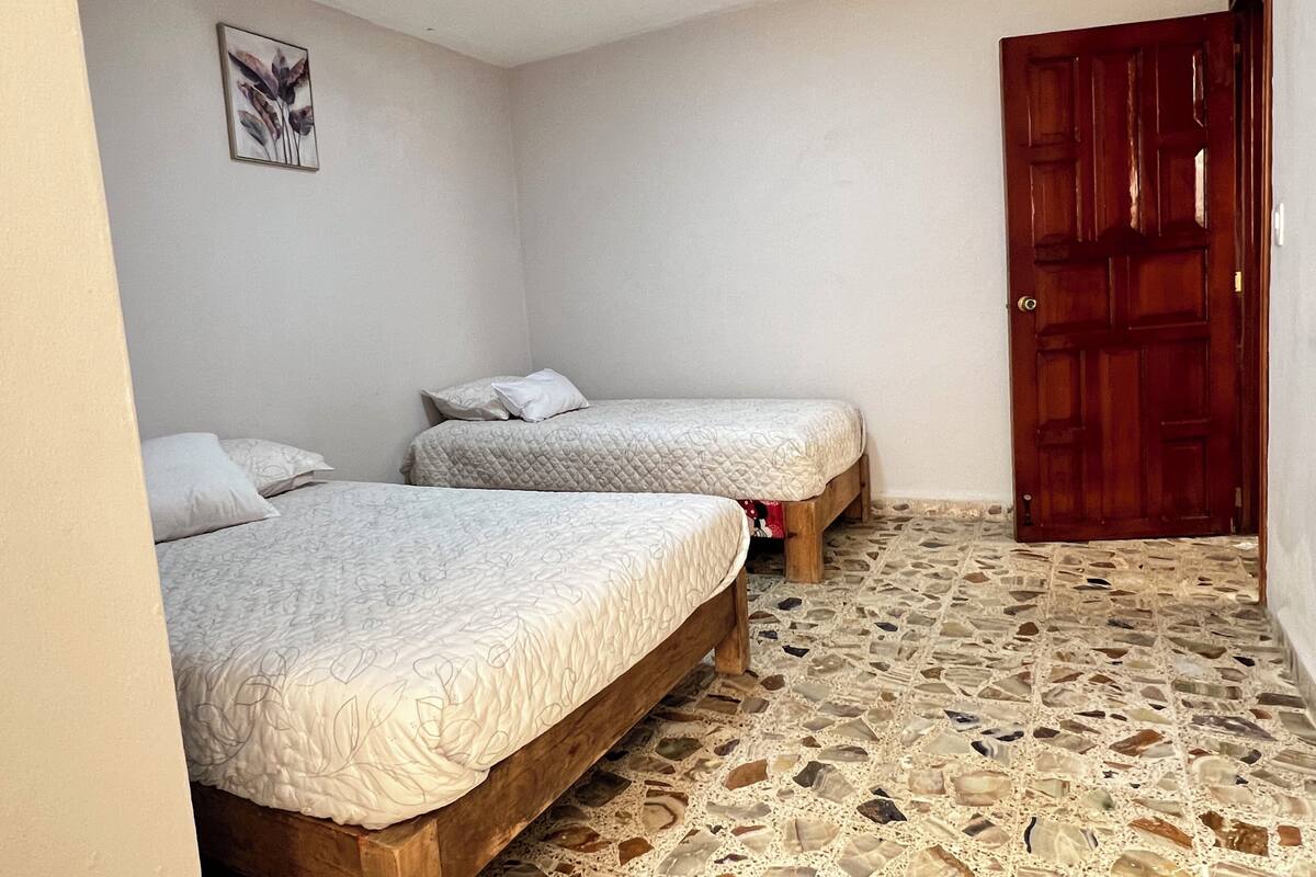 Un dormitori amb dos llits, una porta de fusta i un paviment de mosaic.