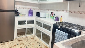 Una cocina con armarios blancos, un refrigerador de acero inoxidable, un microondas, una estufa a gas y un dispensador de agua morado grande.