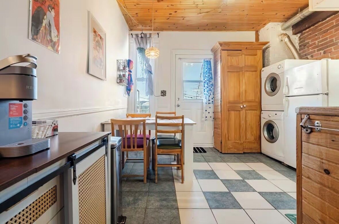 A compact kitchen with a coffee machine, a washing machine, and a dining area with chairs and a table.