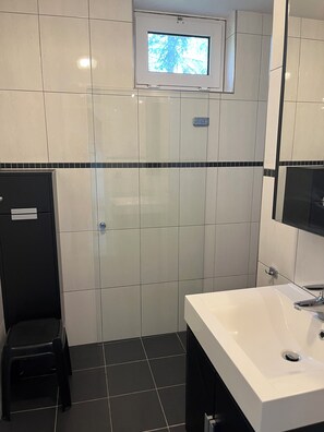 Ein Badezimmer mit weißen Fliesen, einer schwarzen Toilette, einem weißen Waschbecken und einem kleinen Fenster über dem Spiegel.