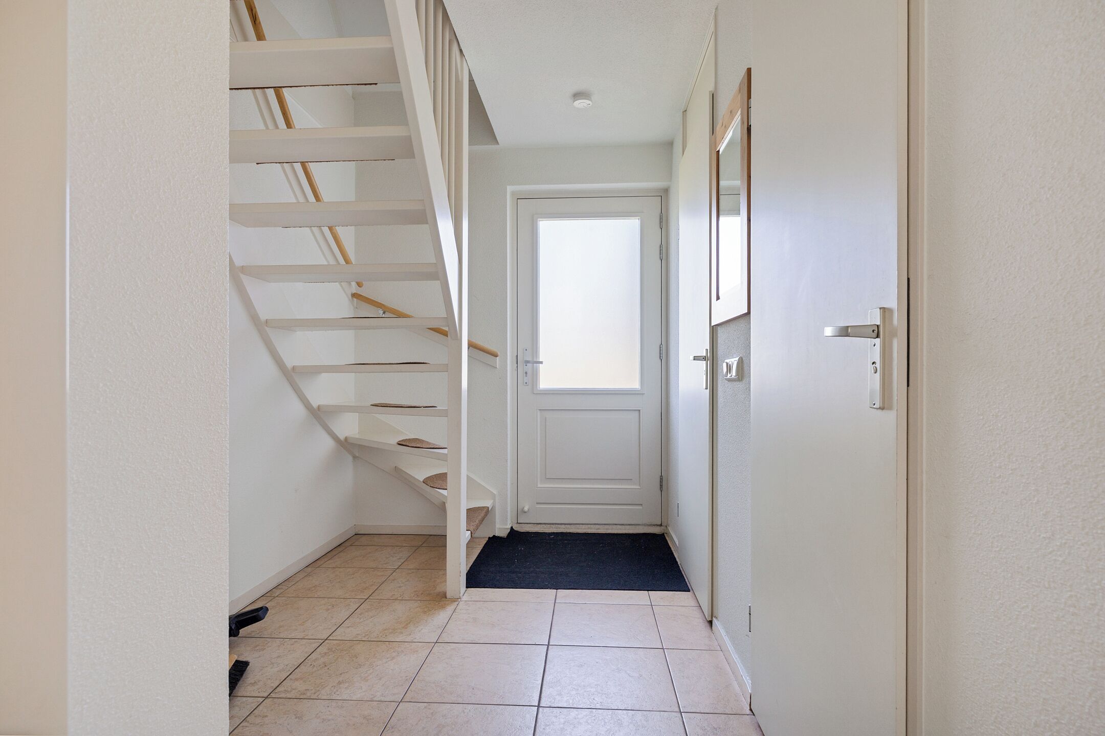 Ein Flur mit Treppe, einer Tür und Fliesenboden.