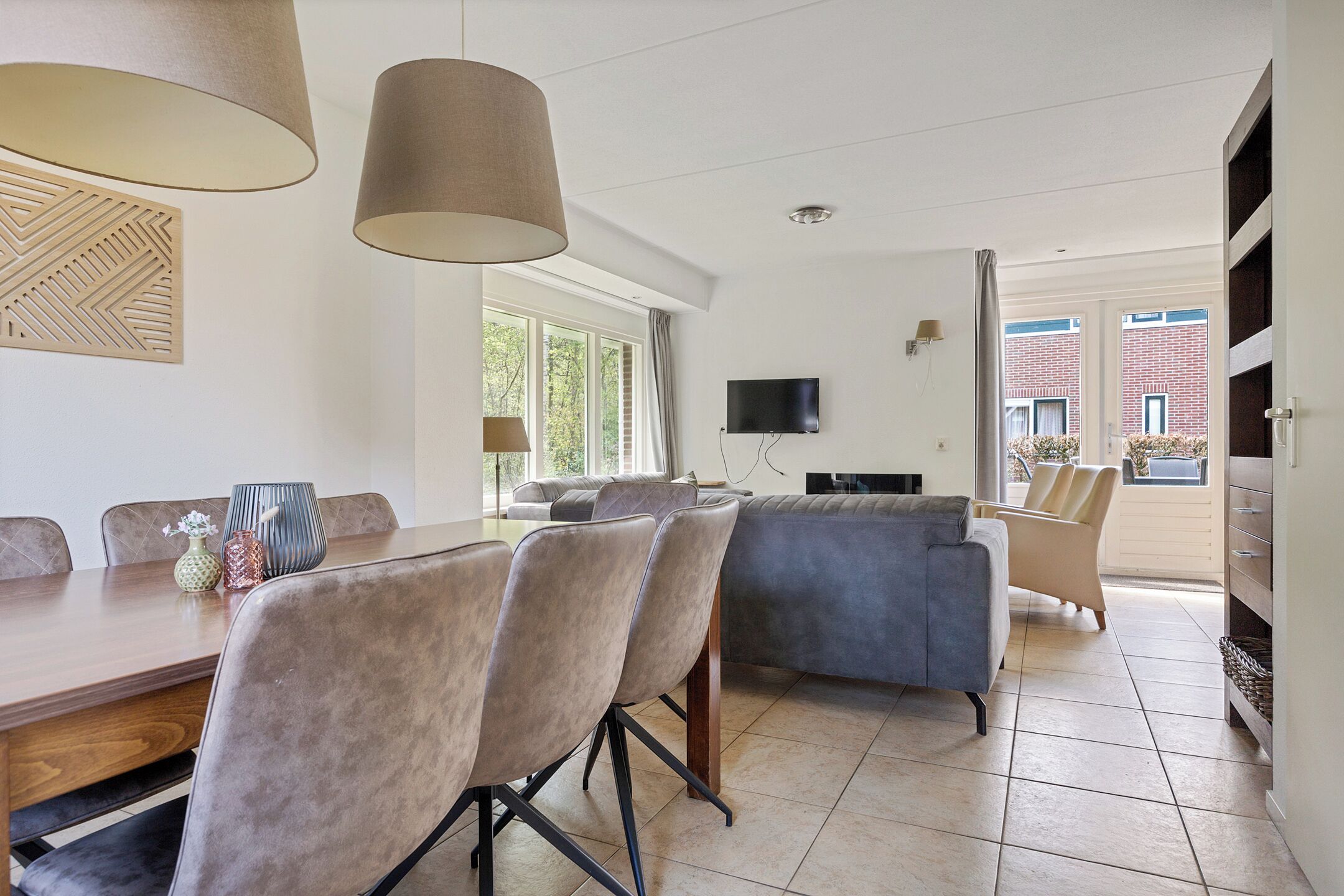 A modern living room with a dining area, a flat-screen TV, and a large window.
