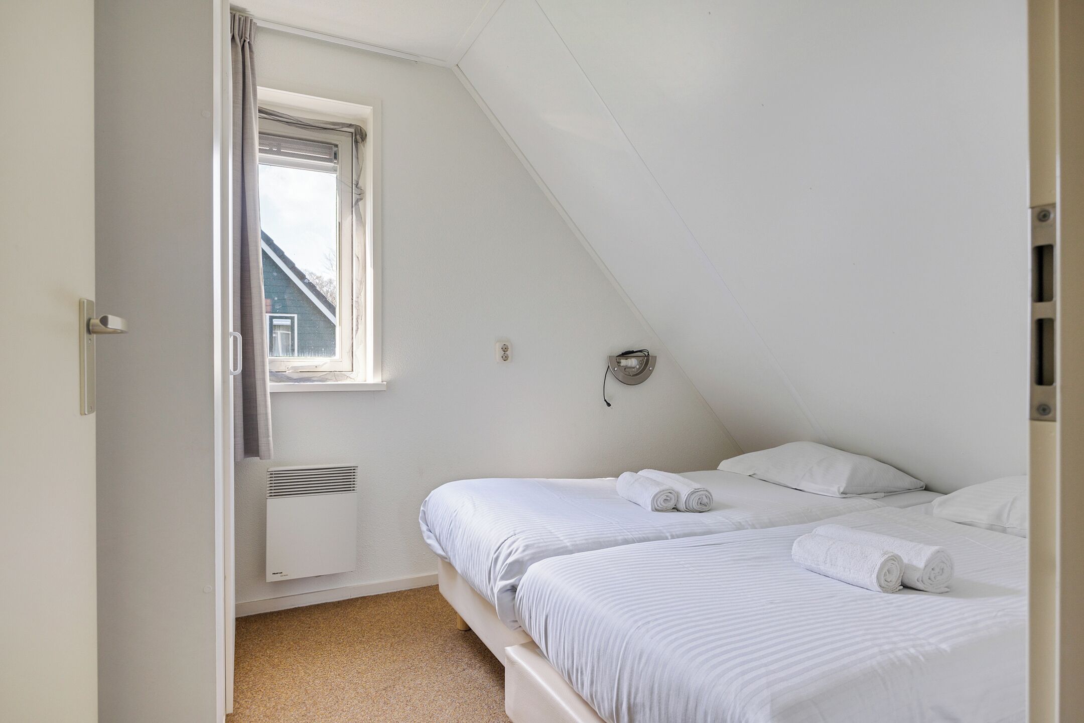 Ein Schlafzimmer mit zwei Betten, einem Fenster, einer Heizung und einer Tür.