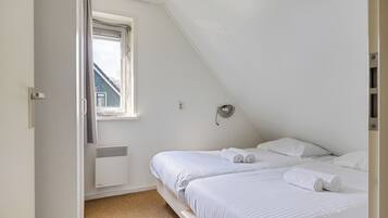 Ein Schlafzimmer mit zwei Betten, einem Fenster, einer Heizung und einer Tür.