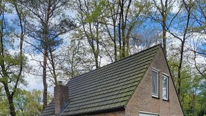 Een klein huis van baksteen met een schuin dak, een terras met zitplaatsen en een gazon.