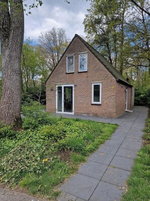 Ein Backsteinhaus mit geneigtem Dach, zwei Fenstern und einer Tür.