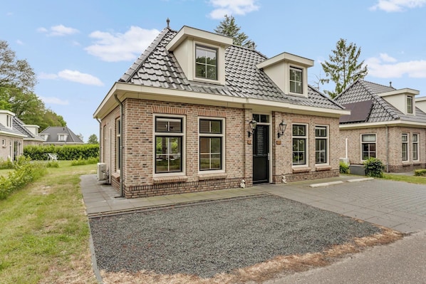 A two-story brick house with a sloped roof, large windows, and a front door. - This charming and distinctive notary’s residence offers the perfect combination of space, comfort, and a natural setting. The detached bungalow accommodates up to 6 people and features a bright living room with French doors opening onto the terrace, (Hoge Hexel)