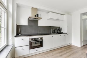 A modern kitchen with white cabinetry, a built-in oven, and a window providing natural light. - This charming and distinctive notary’s residence offers the perfect combination of space, comfort, and a natural setting. The detached bungalow accommodates up to 6 people and features a bright living room with French doors opening onto the terrace, (Hoge Hexel)