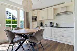 Eine moderne Küche mit weißen Schränken, einem Holztisch und einem großen Fenster.