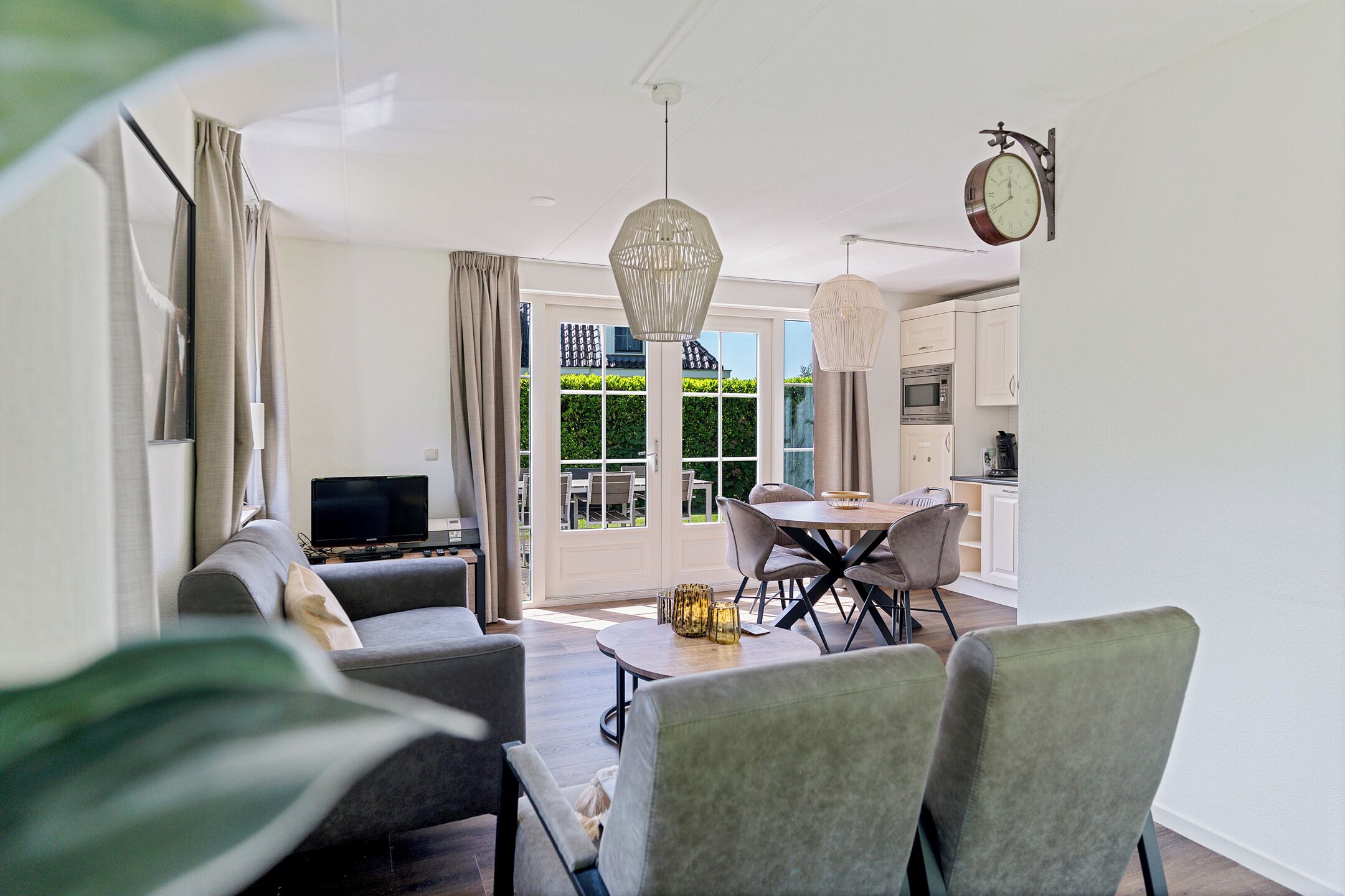 A modern living room with a sofa, dining table, and chairs, a television, and a kitchen in the background.