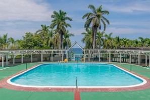 Ein rechteckiger Swimmingpool mit kristallklar blauem Wasser, umgeben von einer grünen Liegefläche und einer weißen Metallkonstruktion.