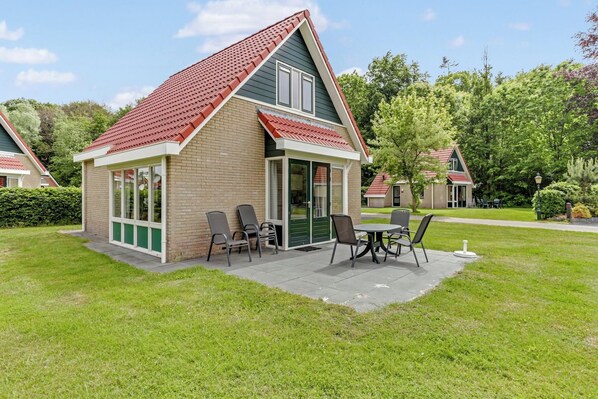 Ein kleines Haus mit rotem Dach, Backsteinfassade und einer Terrasse mit Stühlen und Tisch.