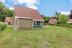 Ein einstöckiges Gebäude mit rotem Ziegeldach, einer Veranda und einem kleinen Garten.