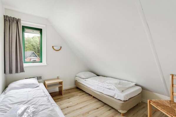 Une petite pièce propre et bien rangée, avec un lit, une chaise, une petite table et une fenêtre avec des rideaux.