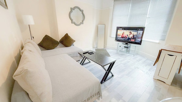 A modern living room with a sofa, a coffee table, a TV, and a window with blinds. - Spacious 4BR House, Garden Retreat, Parking (Wallasey)