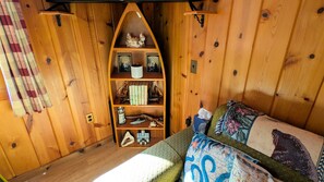 A cozy room with wooden walls, a bookshelf, a bed with a quilt, and a window with curtains.