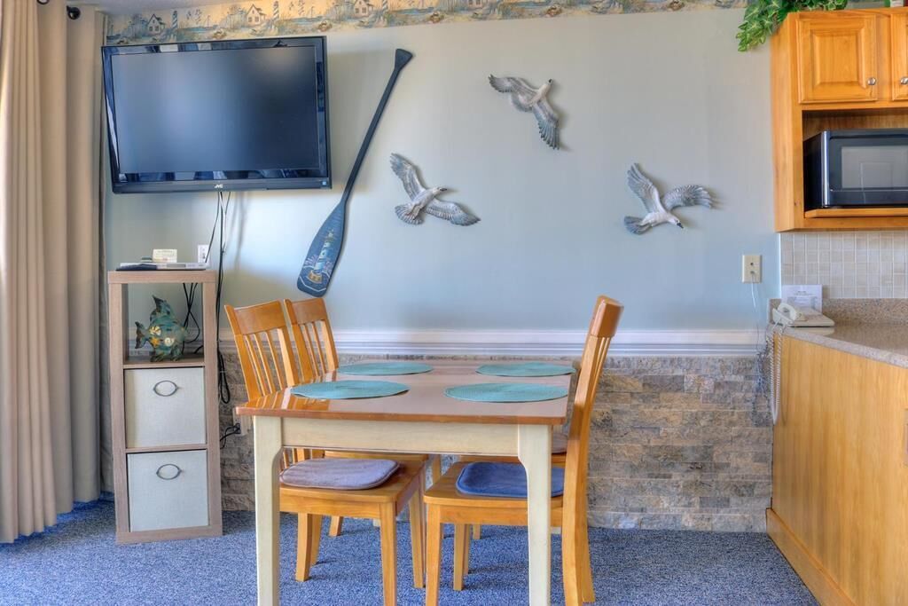Een eethoek met een houten tafel en stoelen, een wandtelevisie en decoratieve wandkunst.