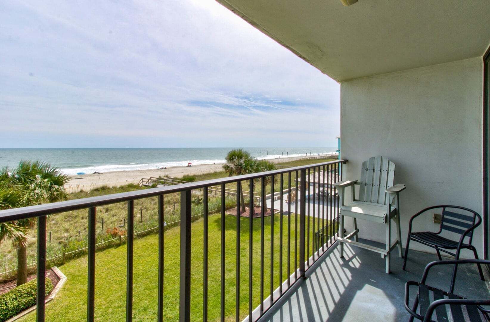 Un balcon avec vue sur la plage, une pelouse et une chaise.