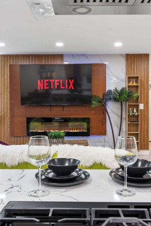 A modern living room with a flat-screen TV, fireplace, and dining setup. - Chic 3BR Hollywood Escape w/ Pool + Private Patio (Los Angeles)