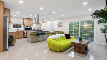 A modern kitchen with a dining area, a bright yellow sofa, and a large window.