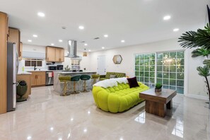 A modern kitchen with a dining area, a bright yellow sofa, and a large window. - Chic 3BR Hollywood Escape w/ Pool + Private Patio (Los Angeles)