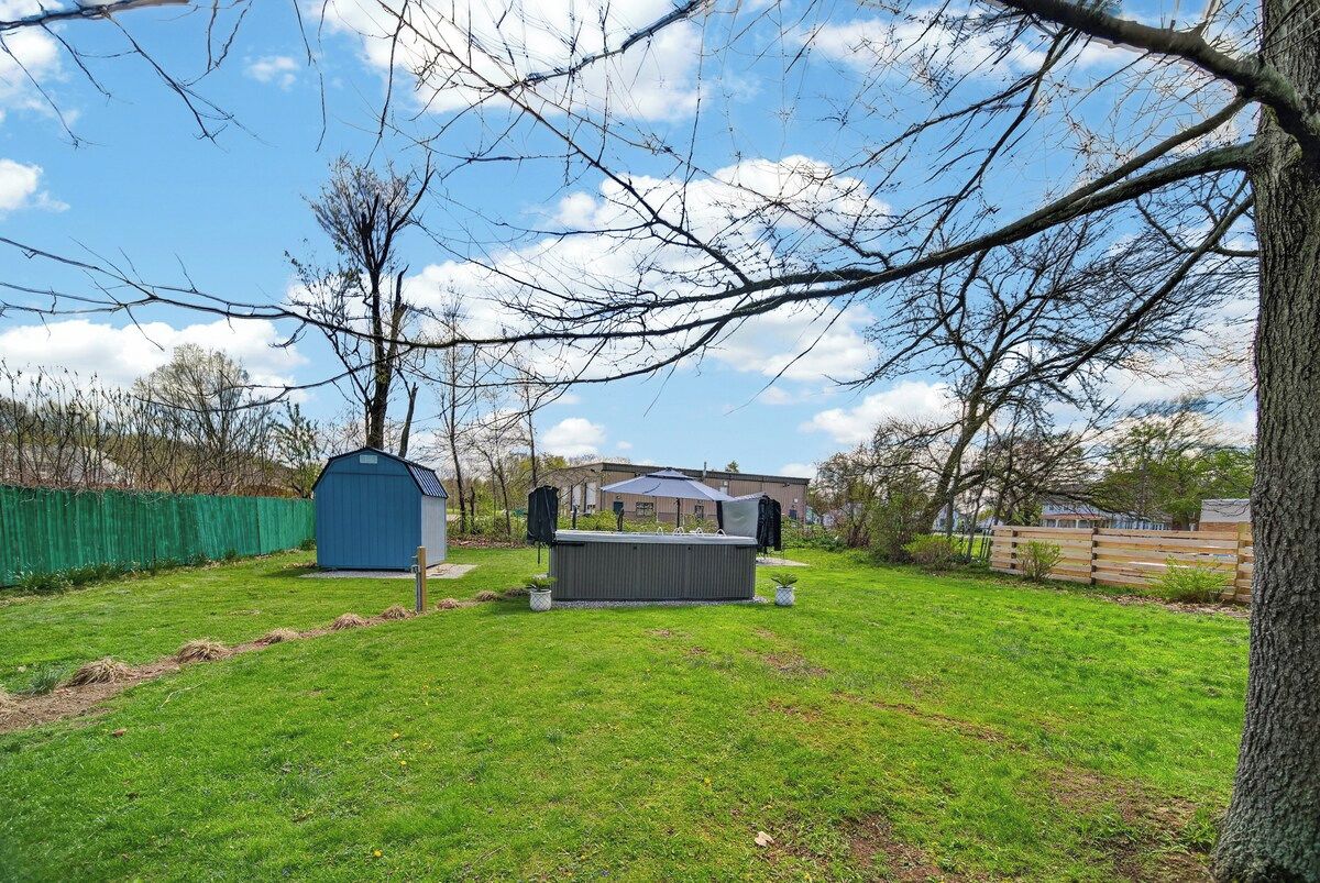 Un jardin avec un abri de jardin, un barbecue et une maison en arrière-plan.