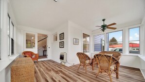 A room with a wooden floor, white walls, wicker furniture, and a ceiling fan.