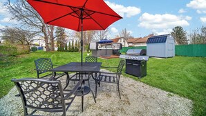 An outdoor patio with a table and chairs, a red umbrella, and a barbecue grill.