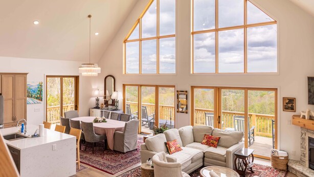 Un espacio habitable espacioso con techo alto, ventanas amplias, chimenea y comedor con mesa y sillas.