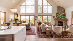 Amplia sala de estar con chimenea, ventanas grandes y comedor con mostrador de cocina.