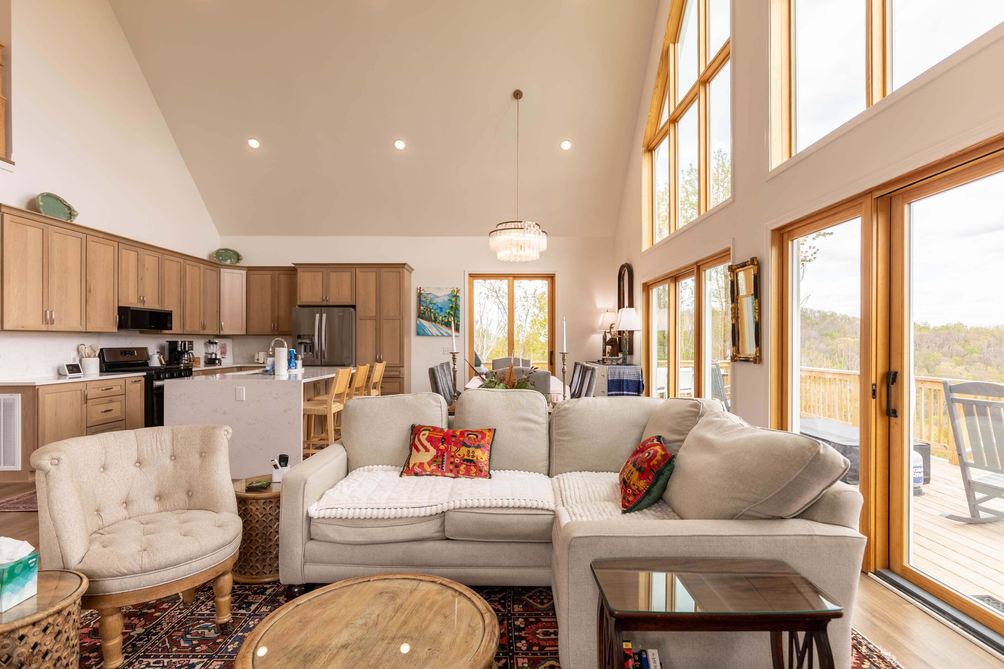 A spacious living area with a sofa, armchair, and coffee table, a kitchen with wooden cabinets, and large windows offering a view.