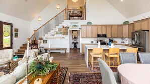 Amplia sala de estar con una escalera que conduce a un altillo, una cocina equipada con electrodomésticos modernos y un comedor con una mesa grande.