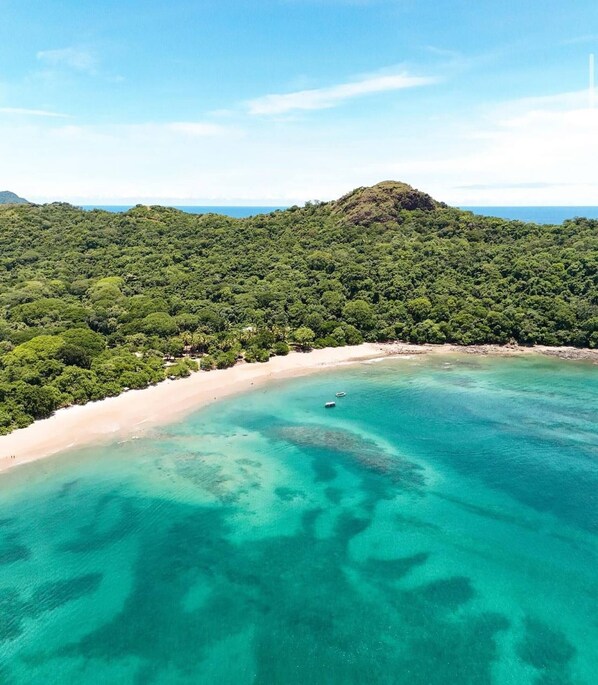 A coastal landscape with a beach, clear turquoise waters, and dense green forested hills. - Mística Natural, A Private Costa Rican Sanctuary (Cabo Velas)