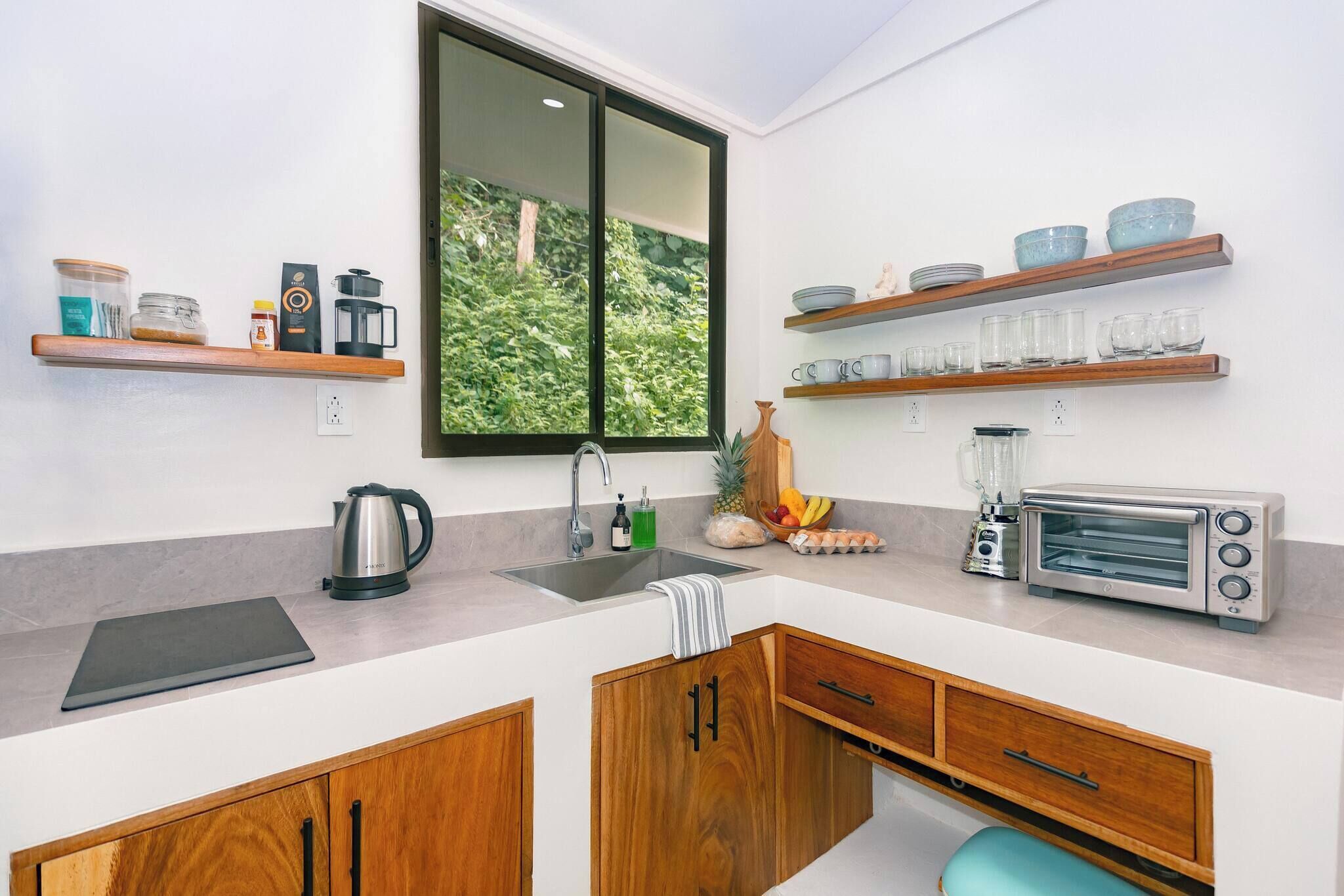 A modern kitchen with a large window, wooden cabinets, a coffee maker, a toaster, and a fruit bowl.