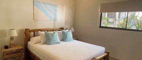 Un dormitorio con una cama de madera, una mesita de noche, aire acondicionado de pared y una ventana con vista a follaje.