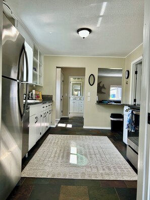 A modern kitchen with stainless steel appliances, a central island, and a view to the dining area. - Cozy 2-bedroom cottage in Anacortes, perfect for a relaxing getaway (Anacortes)