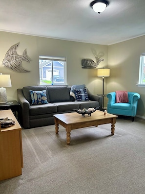 A living room with a grey sofa, a blue armchair, a wooden coffee table, and decorative wall art. - Cozy 2-bedroom cottage in Anacortes, perfect for a relaxing getaway (Anacortes)