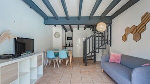 Un espacio habitable moderno con comedor, sofá, televisor y una escalera.
